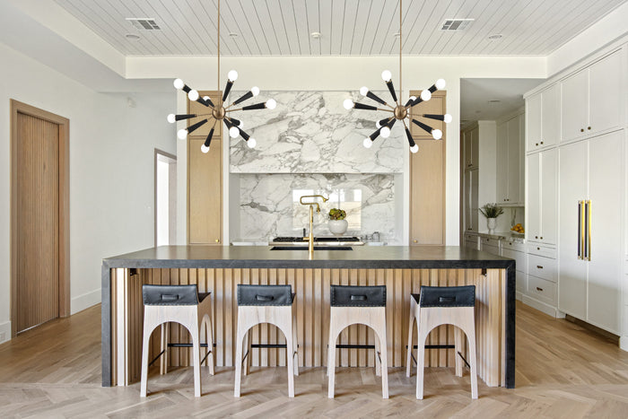 Crystorama Zodiac 34-inch aged brass and black 12-light sputnik chandelier pair over a wood and concrete kitchen island with marble backsplash
