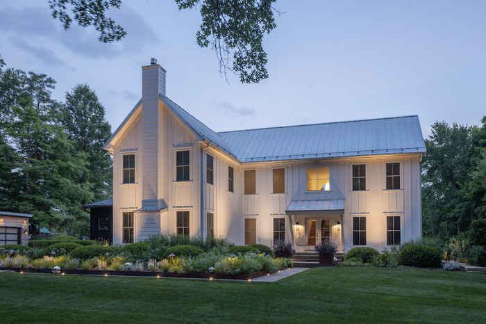 Hinkley Flare 12V stainless steel LED uni-directional well lights uplighting a modern white farmhouse facade and front garden beds at dusk