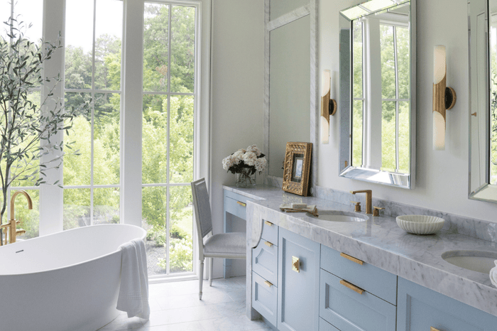 Hinkley Grace 23-inch heritage brass LED vanity with etched opal glass flanking a marble vanity mirror in a light blue bathroom