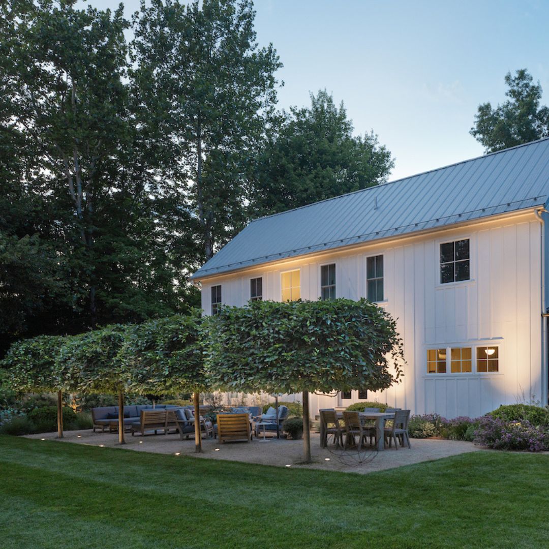 Flat Top Outdoor Landscape Well Light styled in a backyard among trees, positioned near a patio seating area adjacent to a farmhouse.