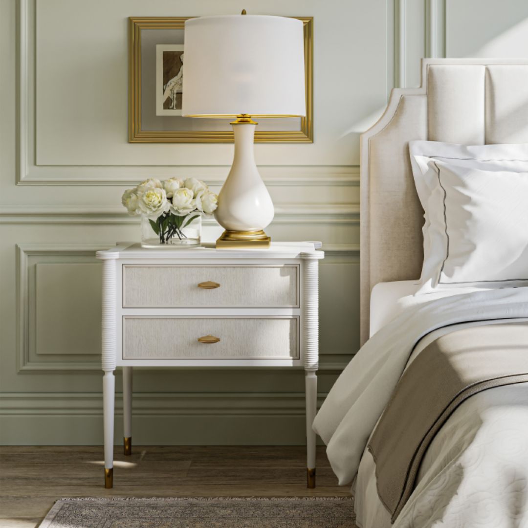 Aster White Nightstand styled with a Lynton Cream Table Lamp in a light green bedroom, accented by artwork behind it and a transitional bed dressed with layered pillows and blankets.