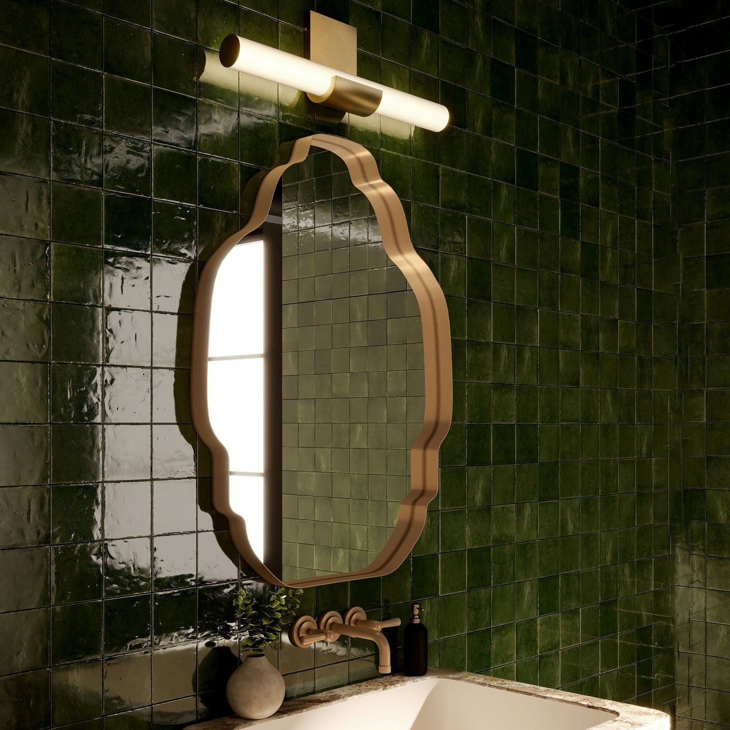 Apollo LED Wall Vanity in a vintage brass finish installed above a brass-framed vanity mirror and sink, set against deep green tiled bathroom walls.