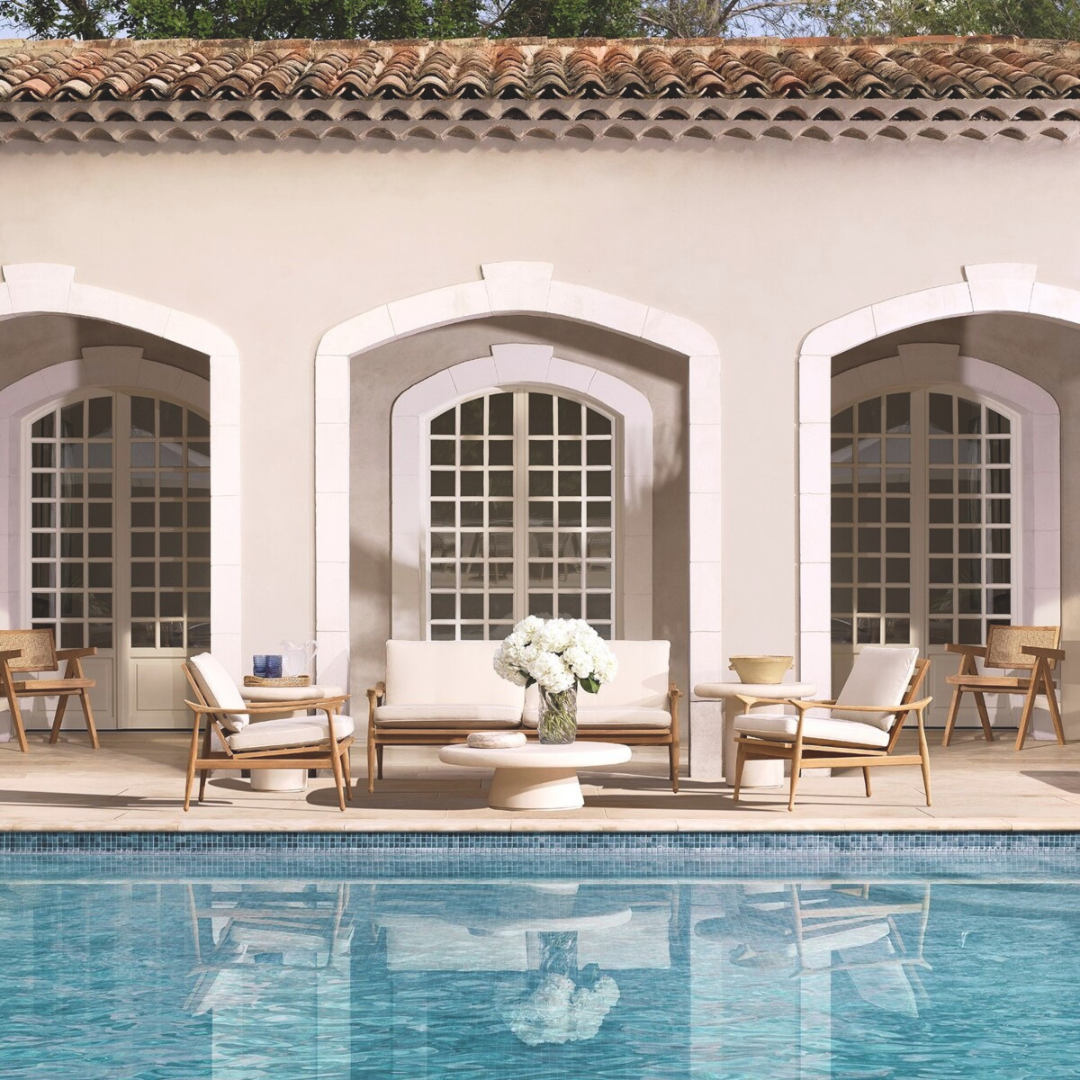 Manzo Outdoor Sofa styled on a poolside patio, flanked by two accent chairs and centered around a coffee table topped with a decorative vase of flowers.