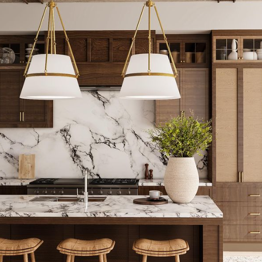 Two Oliver pendants styled in a cozy kitchen with brown wood cabinetry, a marble backsplash and island, three stools, and a touch of greenery.