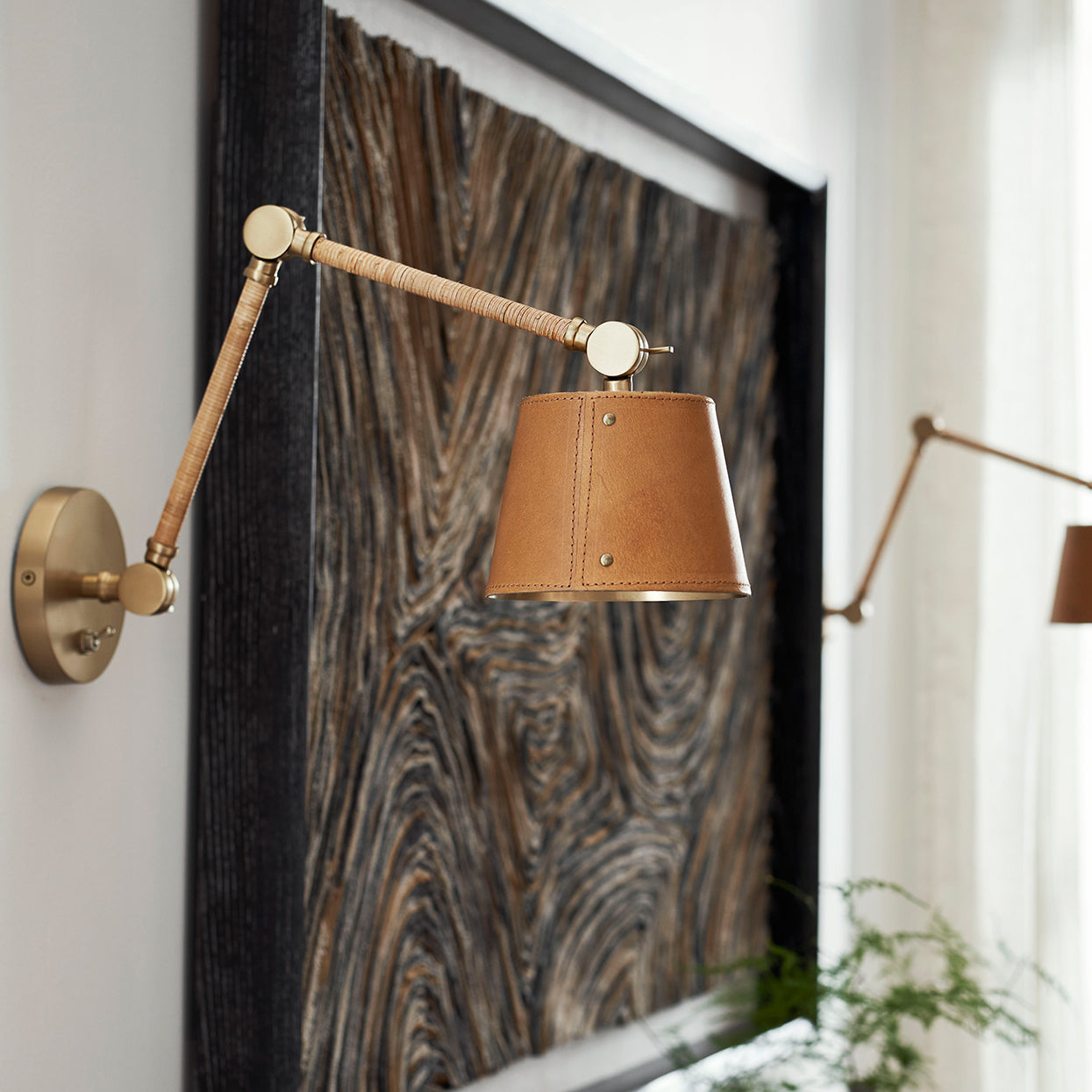 Hendrick Articulating Wall Sconce close up in Antique Brass, Brown Leather Shade finish styled next to a contemporary painting. 