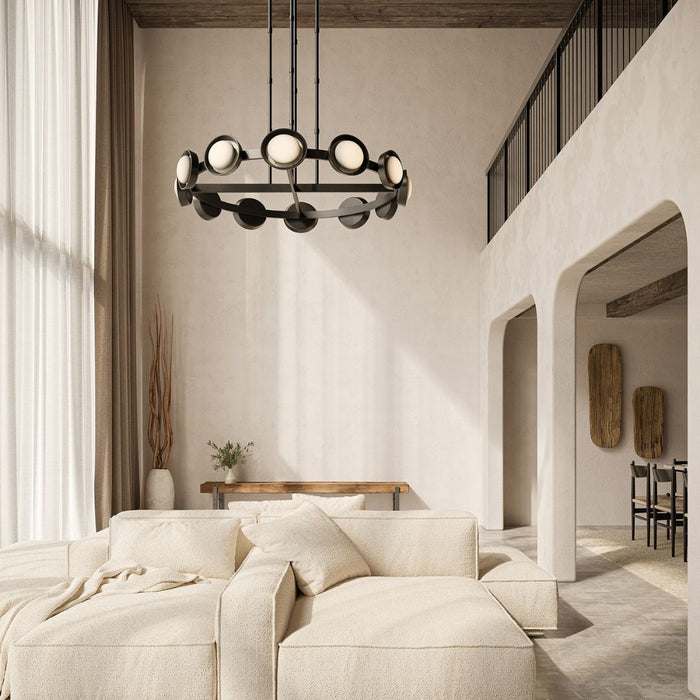 Alonso chandelier suspended in a warm, modern living space with a curved ivory sofa, textured neutral finishes, wood beam ceiling, and arched architectural details.