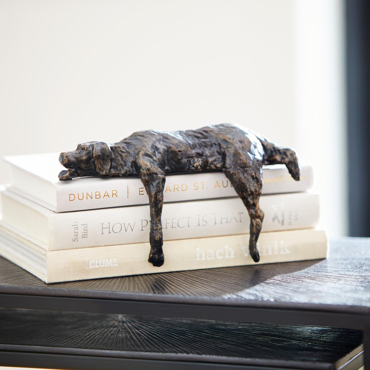 A lazy dog sculpture placed on a console table, resting atop three stacked ivory books.