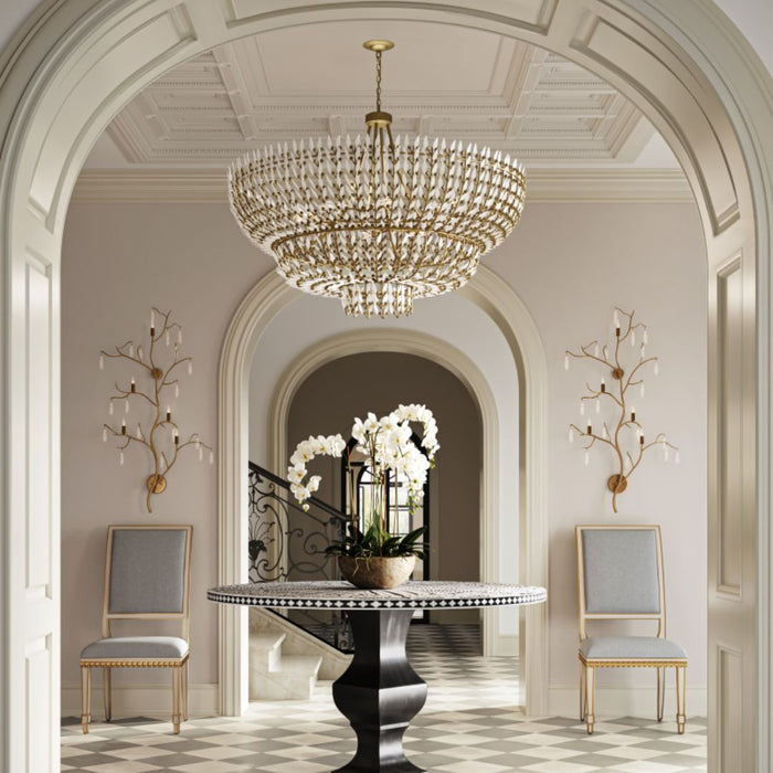 Magnum Opus Grande Chandelier cascading in a grand, arched entryway above a pedestal table with orchids, surrounded by classic architectural details and elegant seating.