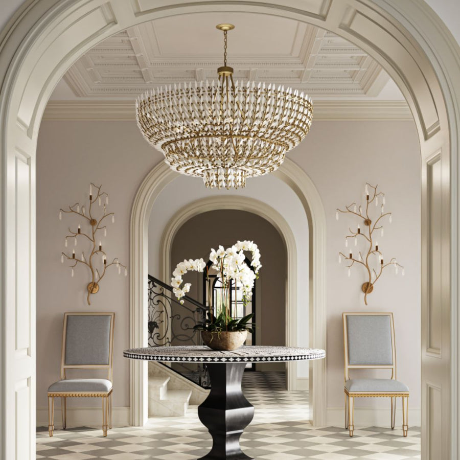Magnum Opus Grande Chandelier cascading in a grand, arched entryway above a pedestal table with orchids, surrounded by classic architectural details and elegant seating.