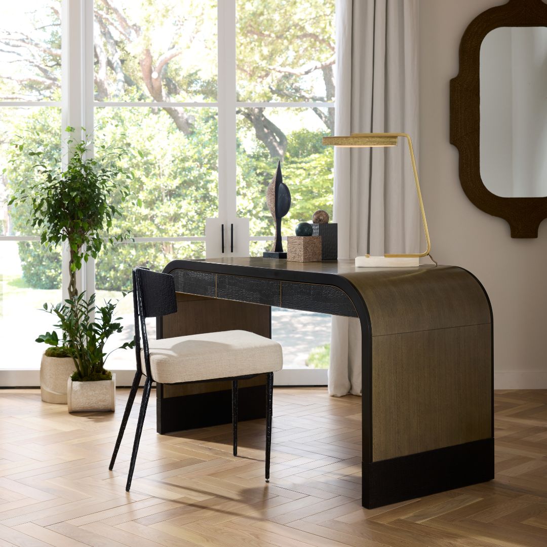 Gaston Desk styled in an office with a desk chair and decorative objects on top, paired with a modern desk lamp, set against grand windows with a wall-mounted mirror and potted plants on the floor.