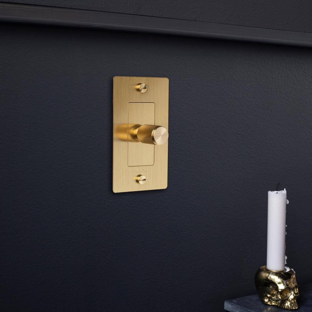 Buster + Punch 1G Metal Dimmer in Brass finish styled on a navy blue painted wall.