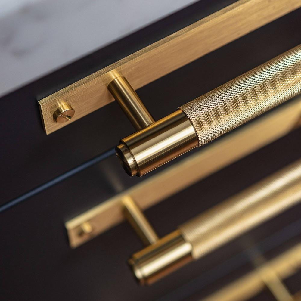 Detail image of the Cross Pull Bar Plate, Medium in a brass finish, mounted on a cabinet drawer.