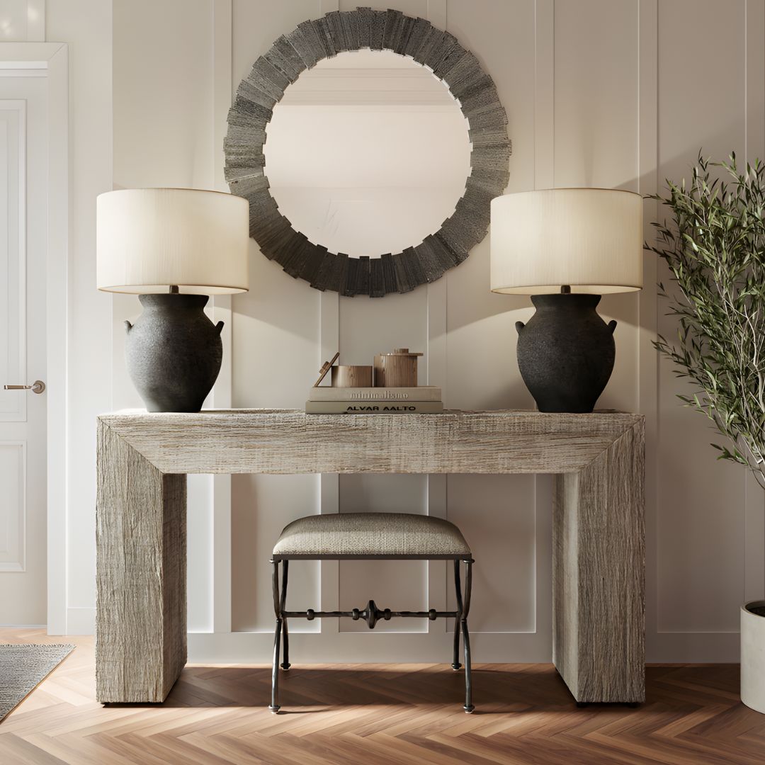 Kanor Whitewash Console Table styled with two Anza Black Table Lamps flanking either side, complemented by decorative accents, set against herringbone wood flooring with a wall-mounted mirror behind and a small ottoman placed beneath.