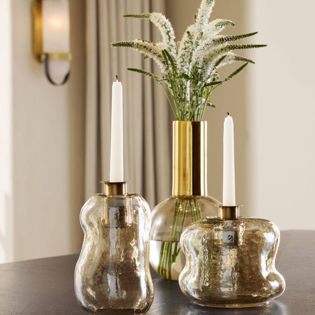 Set of two Hughes Candleholders styled with candles, complemented by a vase filled with greenery.