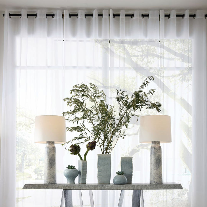 A pair of Heather Table Lamps arranged on a console table, accented with plants and vases, set in front of floor-to-ceiling windows with sheer curtains.