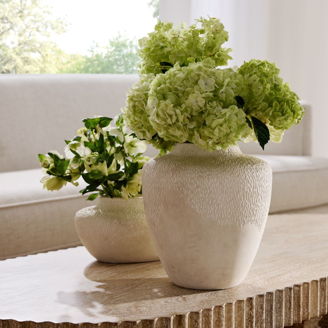 Set of two Freeman Vases styled at the center of a light brown wooden coffee table, featuring white hydrangeas in the larger vase and greenery in the smaller one.