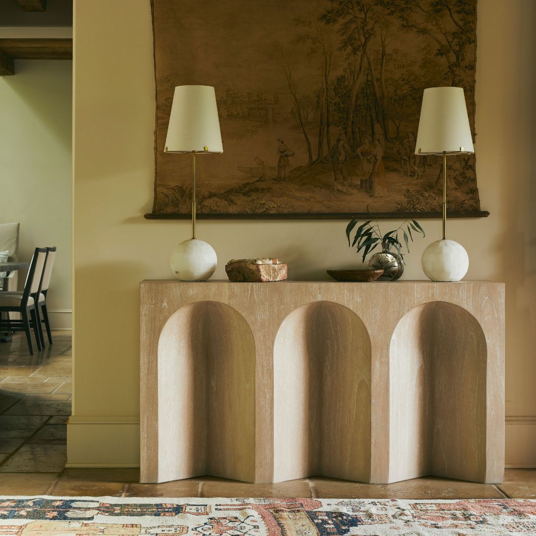 Arlee Console Table styled in a bohemian-inspired entryway, flanked on each end by matching lamps and accented with decorative objects, with a tapestry artwork displayed on the wall behind.