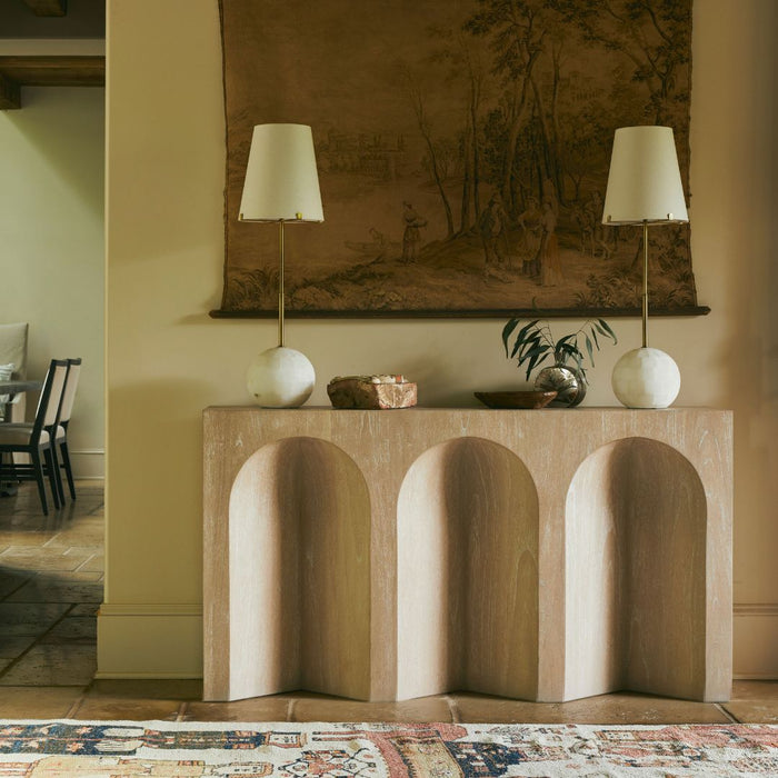 Arlee Console Table styled in a bohemian-inspired entryway, flanked on each end by matching lamps and accented with decorative objects, with a tapestry artwork displayed on the wall behind.