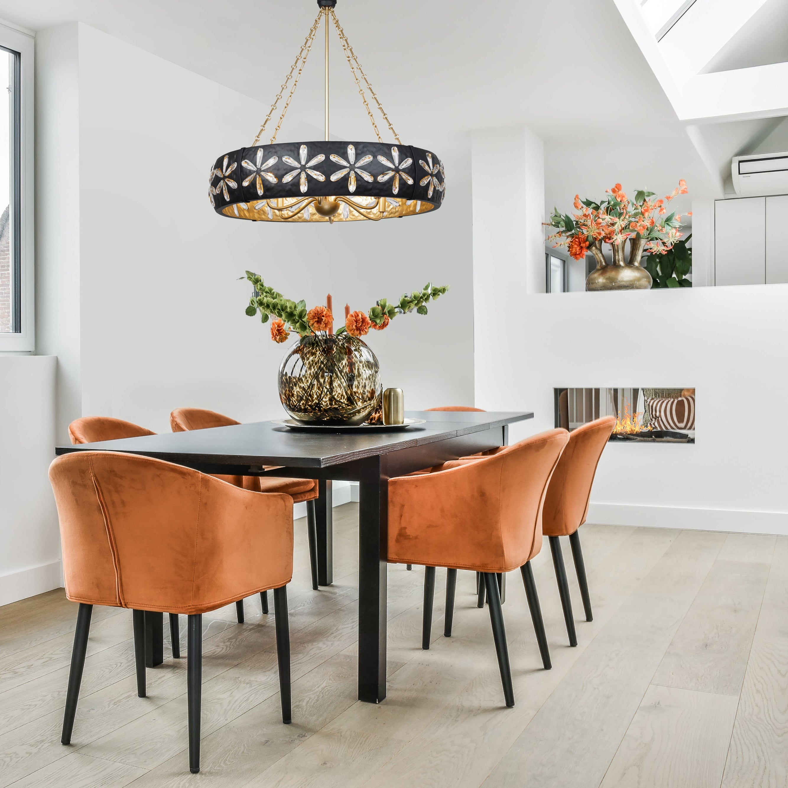 Dining area with a black table, Venice 6-Light Chandelier installed in the center of the table and orange chairs in a bright room.