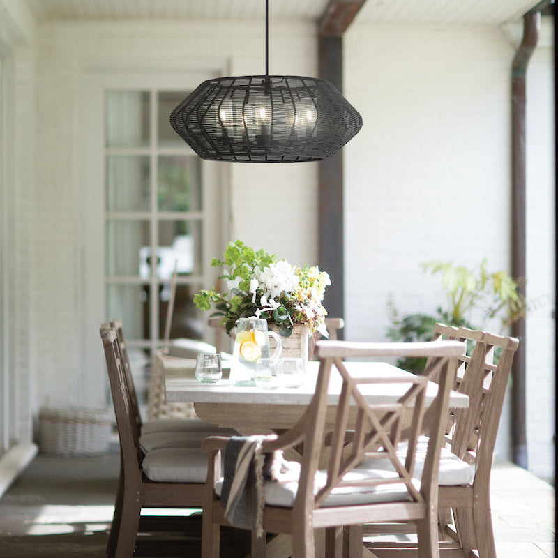Outdoor dining area with wooden table and chairs under a pendant light on a open patio.