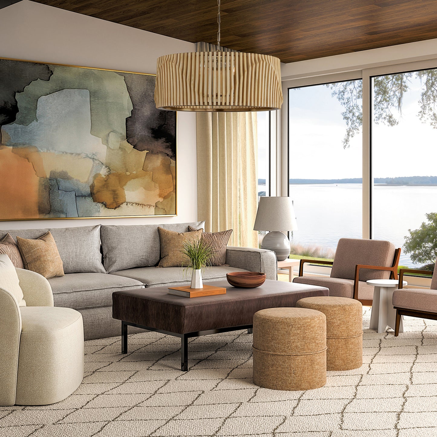 Open living room with gray sectional, leather ottoman, and tan poufs on a trellis rug, facing floor-to-ceiling lake views with the Capital Archer 6-Light Pendant in Light Wood and Matte Black styled in the center.
