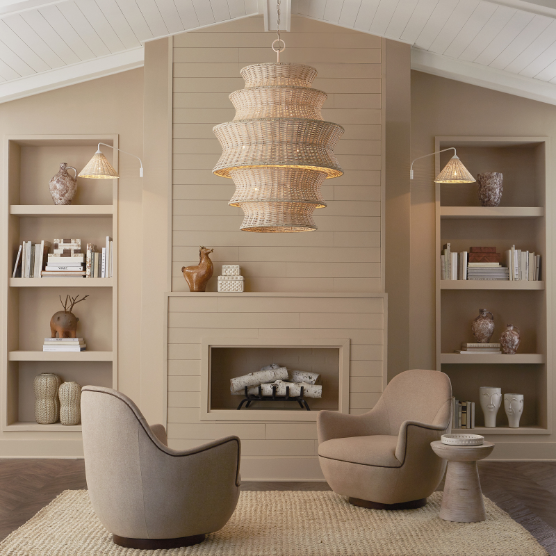 Coastal living room with beige armchairs, a coffee table, rattan style chandelier and decorative shelves.