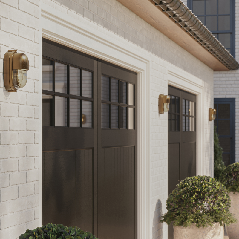 Two black outdoor garage doors with a Maritime Outdoor Sconce flanking each side and green potted plants on both sides.