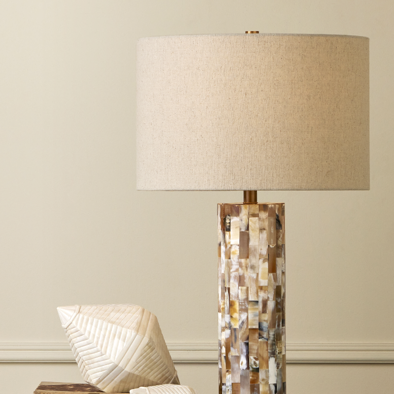 Decorative lamp with mosaic base on a shelf against a neutral wall.