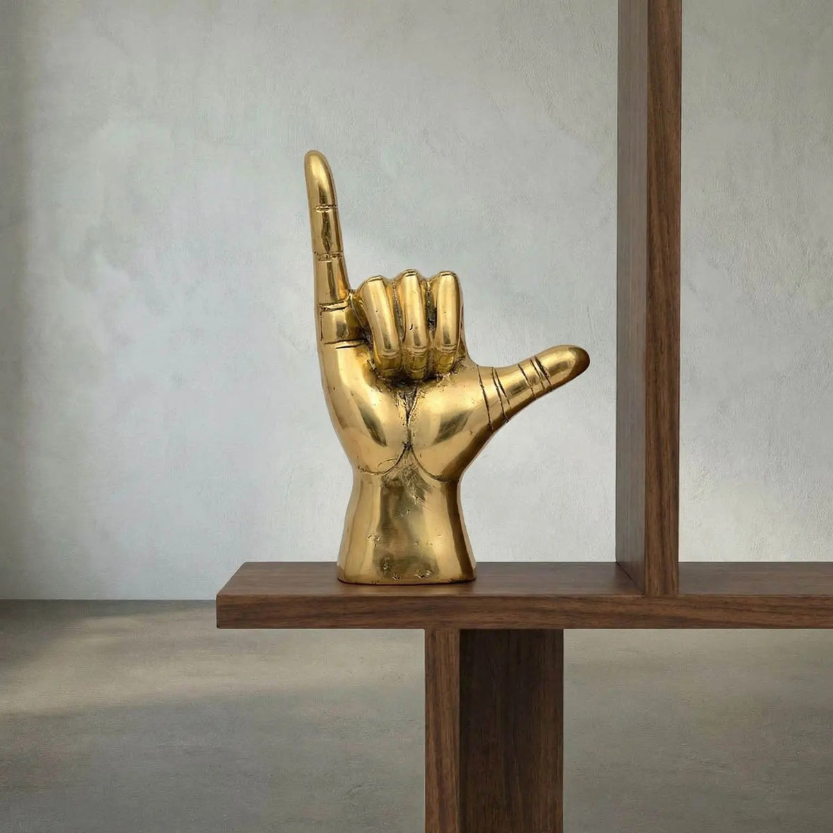Noir Hawaiian Sculpture Antique Brass on a walnut shelf against a pale plaster wall