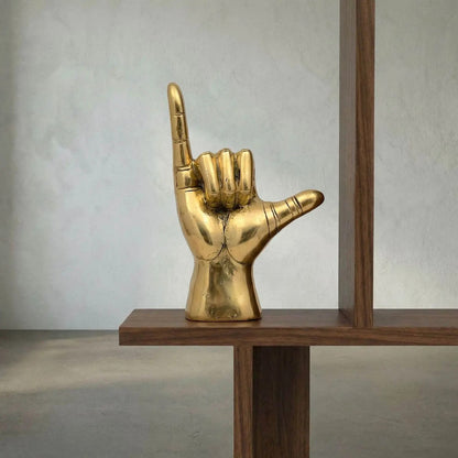 Noir Hawaiian Sculpture Antique Brass on a walnut shelf against a pale plaster wall