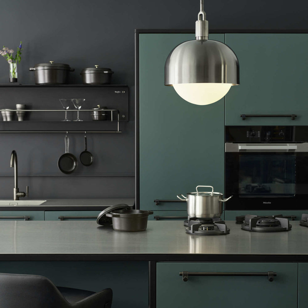 Modern kitchen with dark green cabinets, stainless steel appliances, and the Forked Globe Pendant by Buster and Punch.