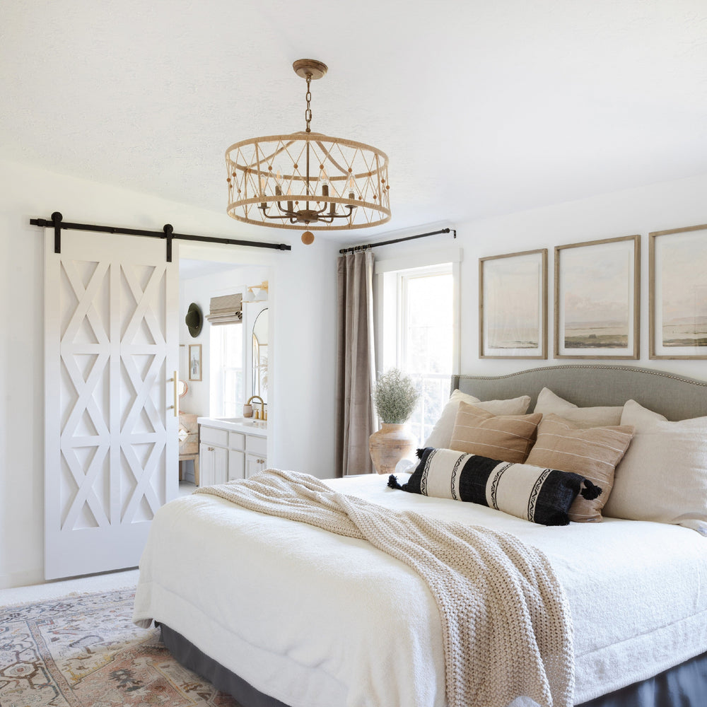 Neatly made bed with decorative pillows and a chandelier in a farmhouse bedroom setting.