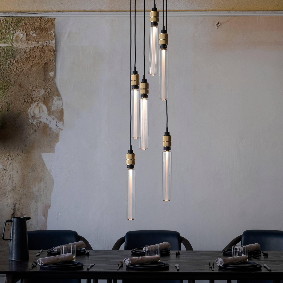 Modern multi port pendant with brass accents by Buster + Punch styled above a dining table with a rustic wall background