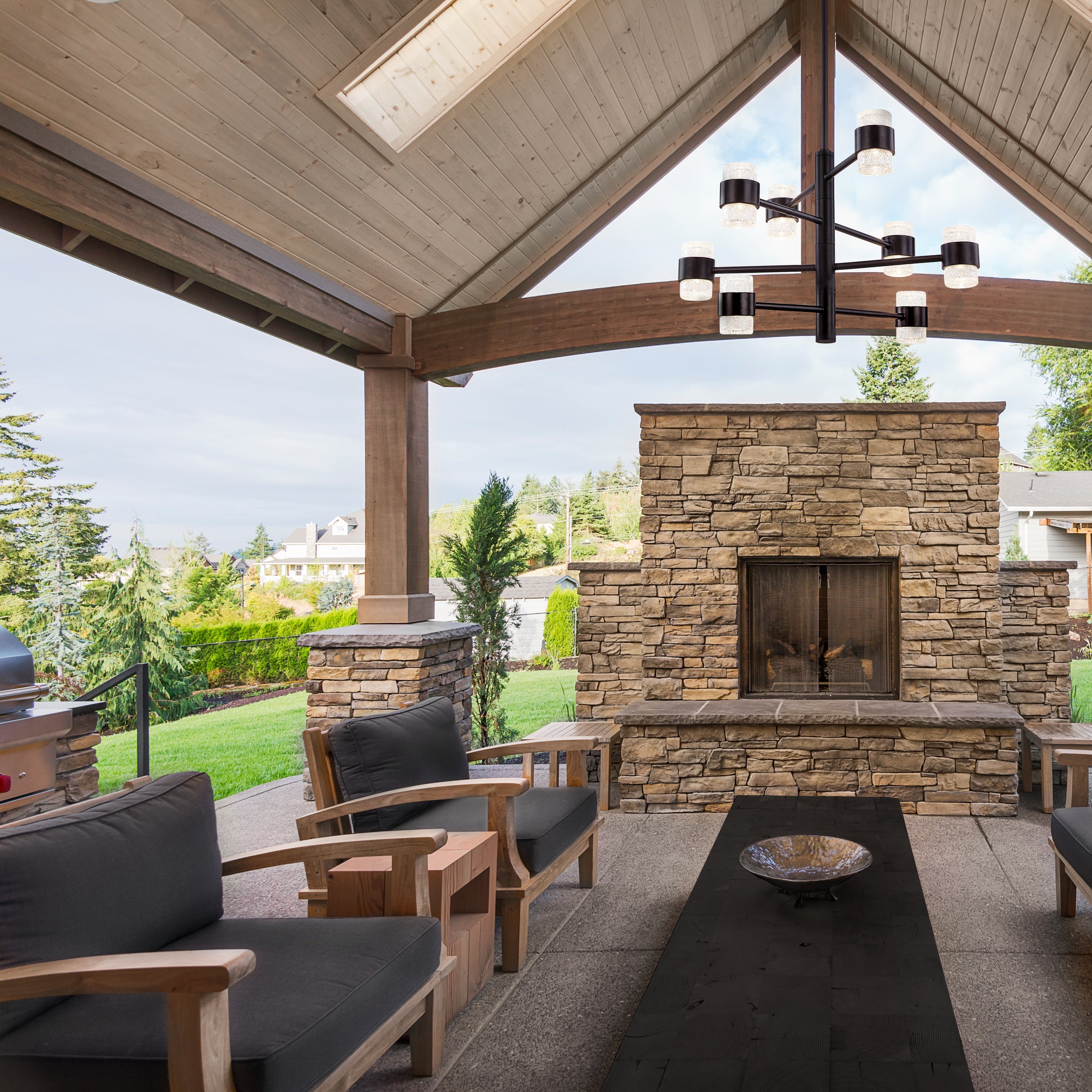 Outdoor patio featuring a stone fireplace, wooden pergola, modern chandelier, and patio furniture.