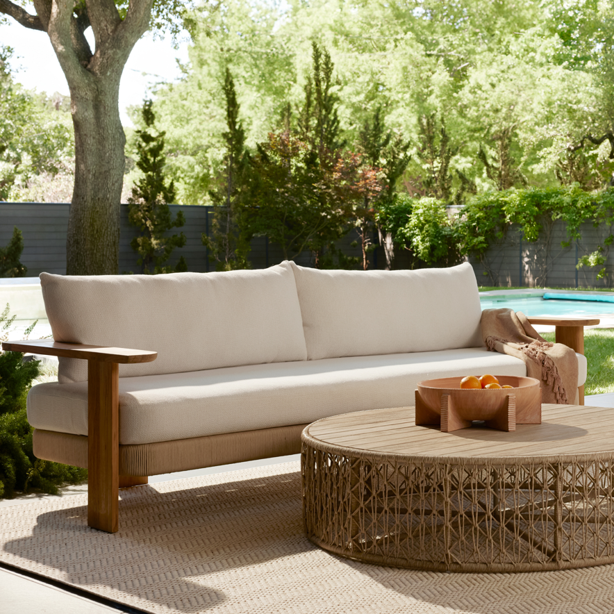 Outdoor patio furniture set with a sofa, armchair, and coffee table in a garden setting.