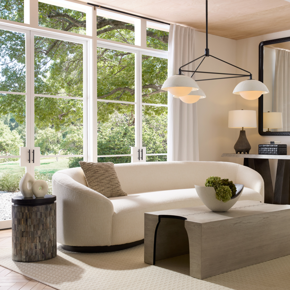 Modern living room with white sofa, coffee table, three light chandelier and decorative elements.