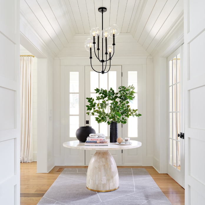 Contemporary entryway with a round marble table, black chandelier, and decorative items.
