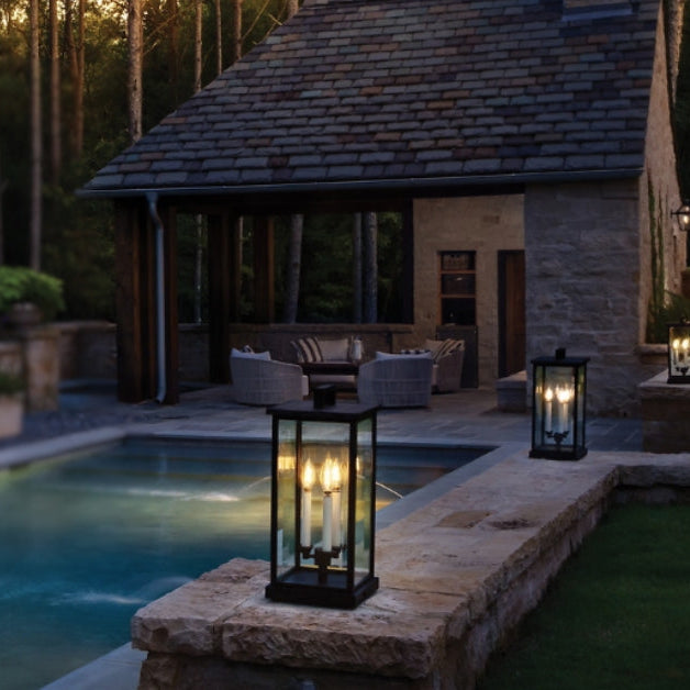 Evening view of a pool area with stone walls, outdoor furniture, and lanterns.
