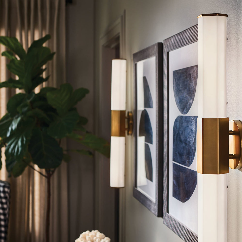 Two facet wall sconces styled on each side of artwork in a hallway.