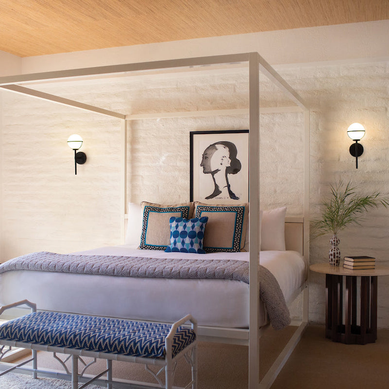 A transitional bedroom with canopy bed, bench, wall art, and two sconces flanking each side of the bed. 