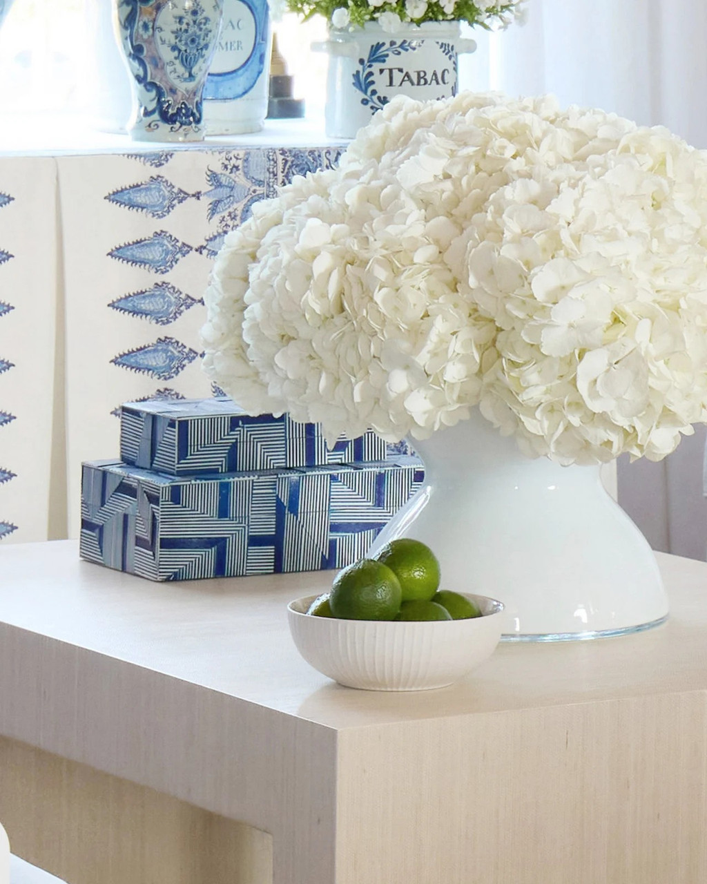 A white vase with flowers and a bowl of limes